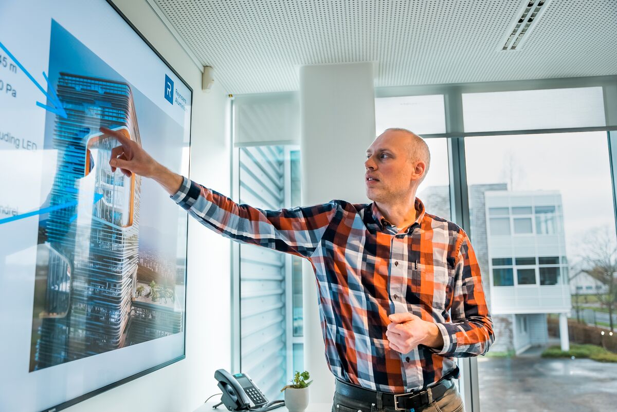 Main in plaid pointing at screen in meeting room