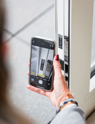 Hand holding smartphone near QR code on white window profile.